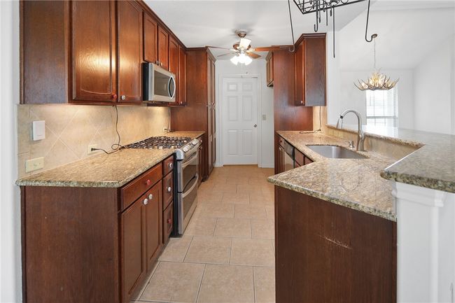 Kitchen with appliances with stainless steel finishes, a ceiling fan, tasteful backsplash, and stone countertops | Image 7