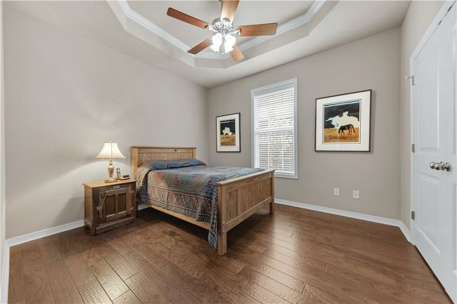 Bedroom featuring a raised ceiling, dark wood-style flooring, baseboards, crown molding, and ceiling fan | Image 25