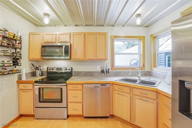 Kitchen with stainless steel appliances, light brown cabinets, tile counters, and light wood finished floors | Image 17