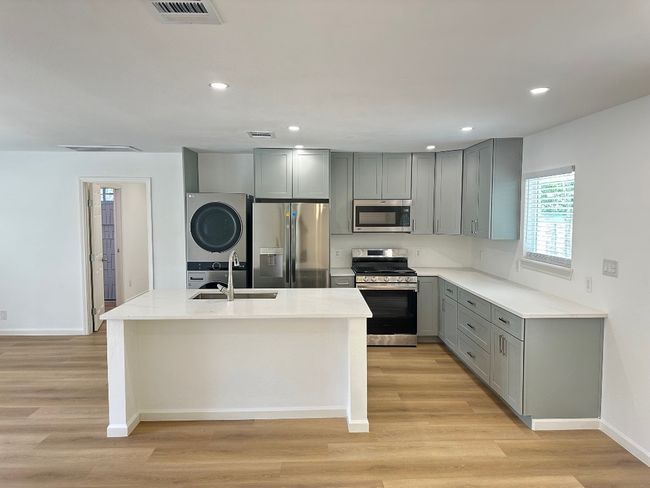 Kitchen with appliances with stainless steel finishes, gray cabinets, a sink, stacked washer / drying machine, and light wood-type flooring | Image 9