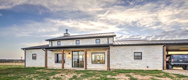 Back of property featuring a standing seam roof, stone siding, metal roof, a carport, and a chimney | Image 4