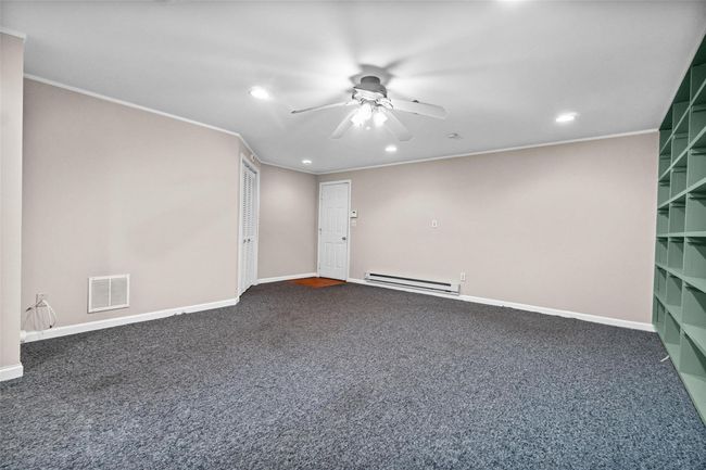 Empty room with a baseboard heating unit, a ceiling fan, recessed lighting, dark colored carpet, and crown molding | Image 26