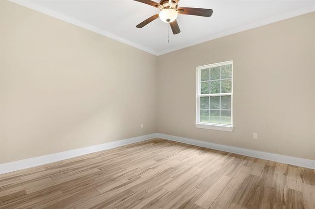 This room features neutral-colored walls, light wood flooring, a ceiling fan with lighting, and a window that lets in natural light, creating a bright and inviting atmosphere. | Image 20