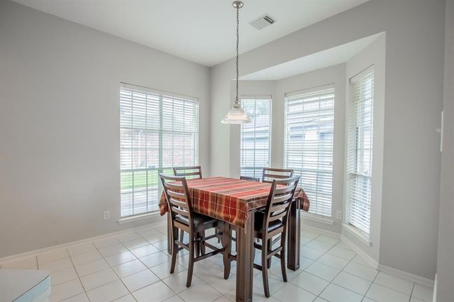 This bright breakfast area features large windows with blinds, offering ample natural light. The space has tiles flooring and neutral walls, creating an inviting and airy atmosphere. | Image 26