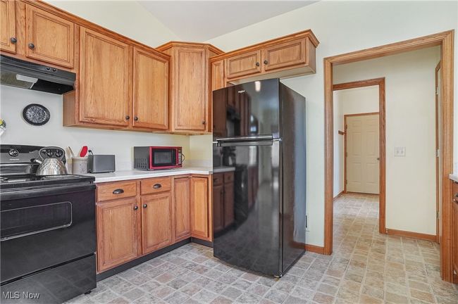 Kitchen with brown cabinets, light countertops, under cabinet range hood, stove, and freestanding refrigerator | Image 23
