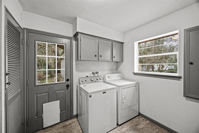 This photo showcases a bright laundry room with a washer and dryer, featuring gray cabinetry and trim. The room has a clean and functional design with light tone walls and flooring. | Image 17