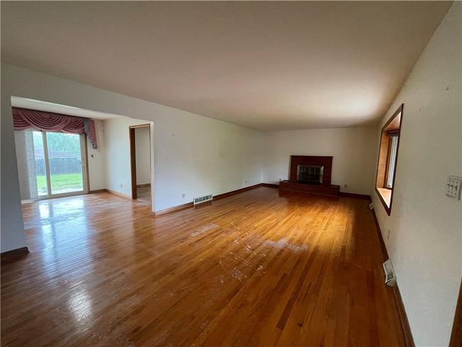 Unfurnished living room featuring a brick fireplace, visible vents, baseboards, and wood-type flooring | Image 7