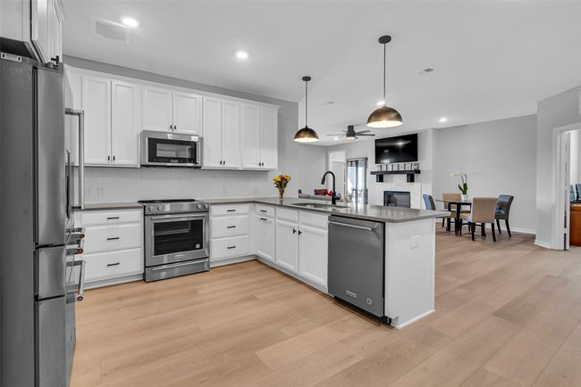 Kitchen featuring white cabinets, appliances with stainless steel finishes, a sink, a glass covered fireplace, and a peninsula | Image 4