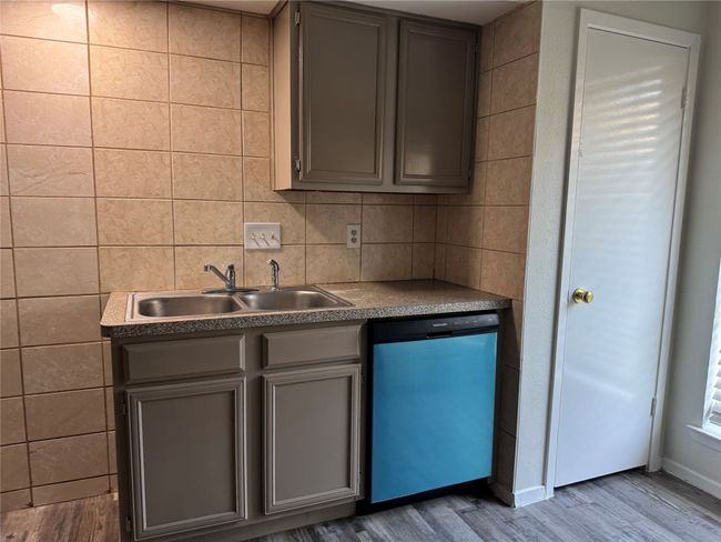 Kitchen with dishwashing machine, a sink, wood finished floors, gray cabinetry, and tile walls | Image 7
