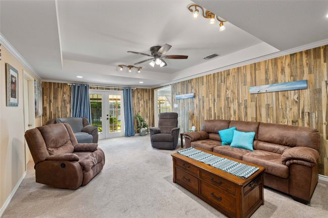 Living area featuring light colored carpet, wooden walls, a raised ceiling, a ceiling fan, and french doors | Image 20