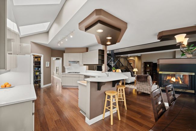 Kitchen featuring white gas cooktop, open shelves, white cabinetry, a skylight, and a multi sided fireplace | Image 14