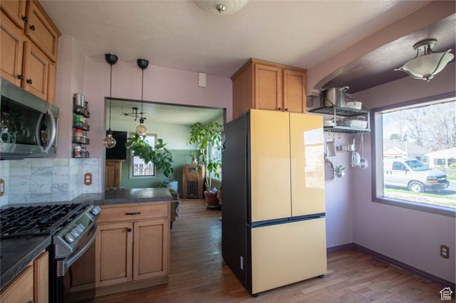Kitchen featuring tasteful backsplash, light wood-type flooring, dark countertops, and stainless steel appliances | Image 7