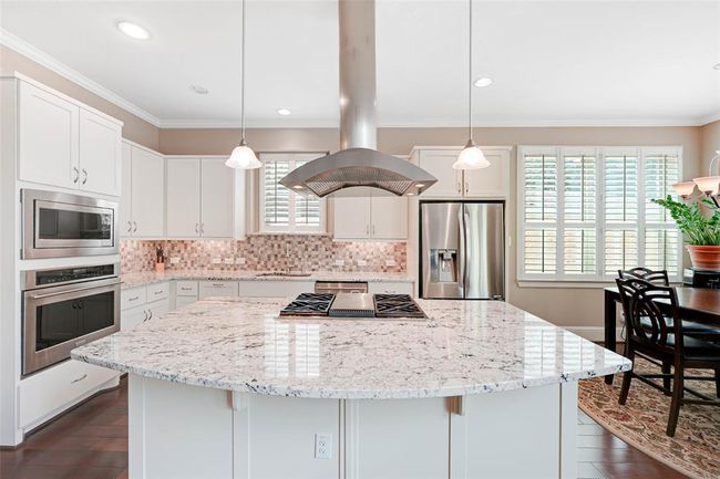 Bright and spacious kitchen featuring a large granite island with 4- Burner gas cooktop and sleek stainless steel vent hood. | Image 10