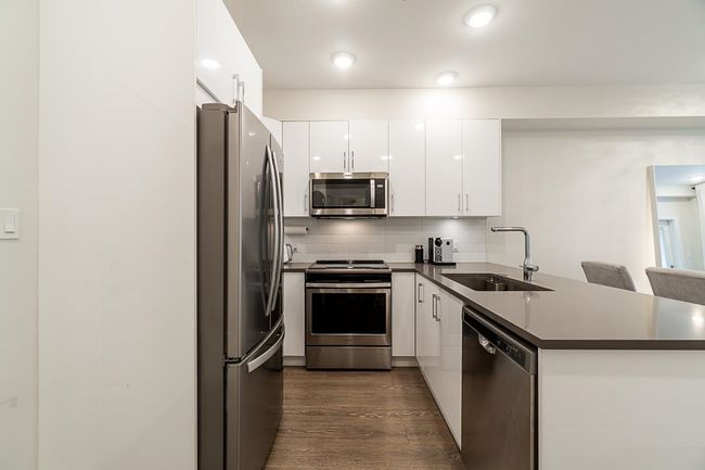 Kitchen with dark countertops, a sink, white cabinets, a peninsula, and appliances with stainless steel finishes | Image 14