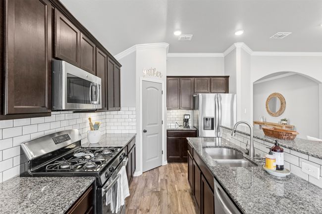 Kitchen with stainless steel appliances, a gas stove, granite countertops, ornamental molding, wood like tile flooring, and dark brown cabinetry | Image 27