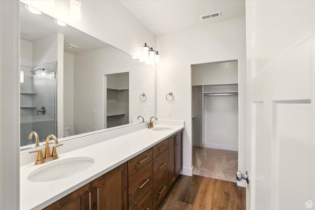 Full bath featuring double vanity, a walk in closet, toilet, wood finished floors, and a shower | Image 17