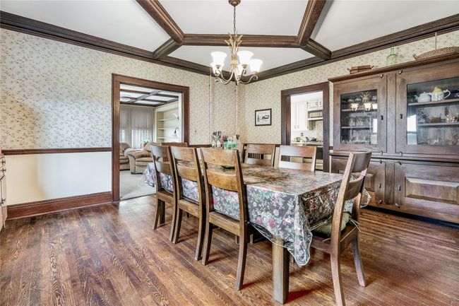 Dining area featuring dark wood-style flooring, a notable chandelier, coffered ceiling, wallpapered walls, and crown molding | Image 16
