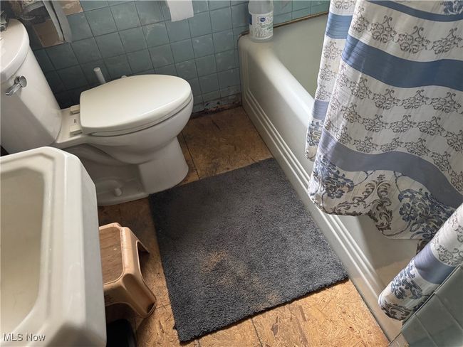 Full bathroom featuring toilet, curtained shower, and tile walls | Image 10