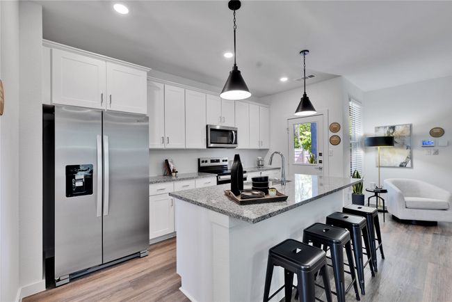 Kitchen with stainless steel appliances, visible vents, white cabinets, light wood finished floors, and an island with sink | Image 12