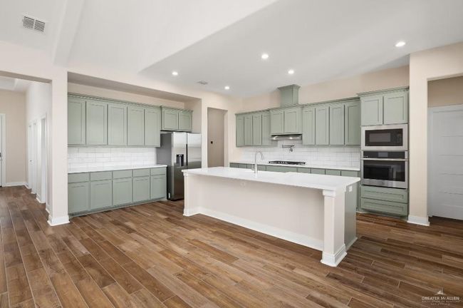 Kitchen featuring dark wood-style flooring, an island with sink, light countertops, backsplash, and appliances with stainless steel finishes | Image 4