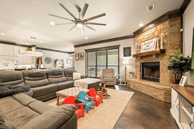 Living area featuring concrete flooring, ornamental molding, a ceiling fan, recessed lighting, and a stone fireplace | Image 4