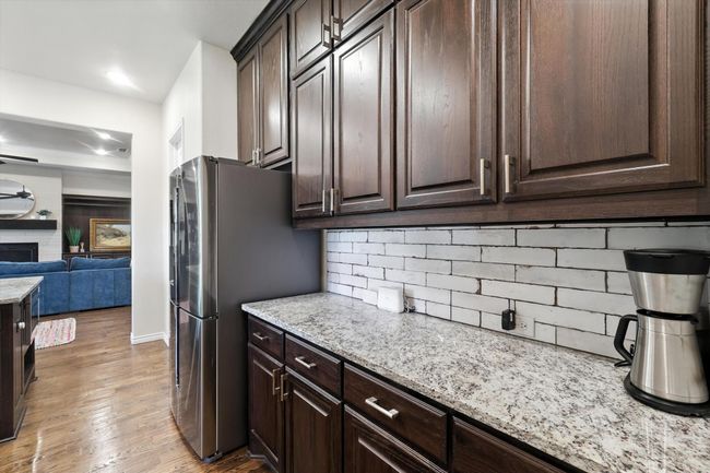 Kitchen featuring dark brown cabinets, decorative backsplash, light wood-type flooring, light stone counters, and freestanding refrigerator | Image 16