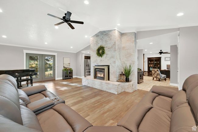 Living room with a brick fireplace, crown molding, lofted ceiling, ceiling fan, and light hardwood / wood-style flooring | Image 9