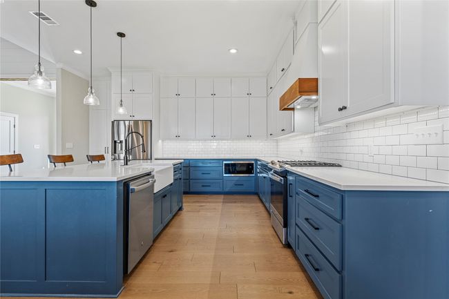 Kitchen with crown molding, blue cabinetry, white cabinets, visible vents, and stainless steel appliances | Image 8