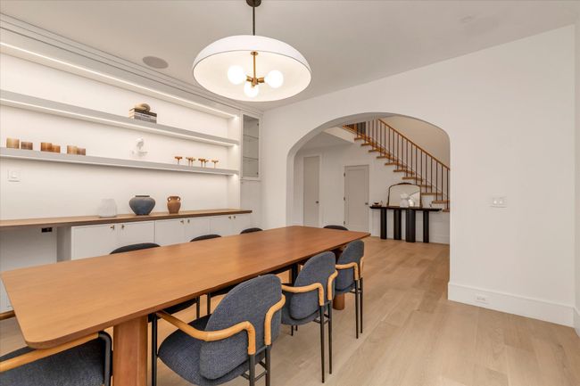 Dining space with arched walkways, light wood-style floors, stairway, and a chandelier | Image 4