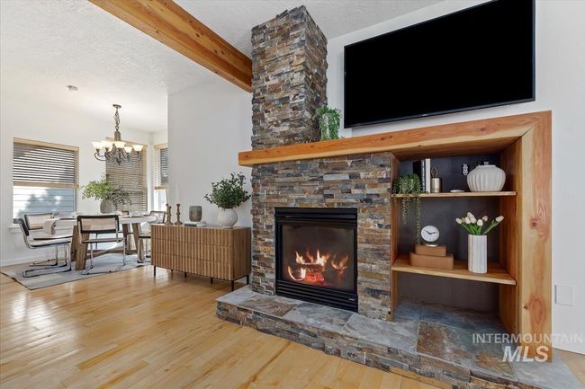 Living area featuring beam ceiling, wood finished floors, a stone fireplace, a textured ceiling, and a chandelier | Image 15