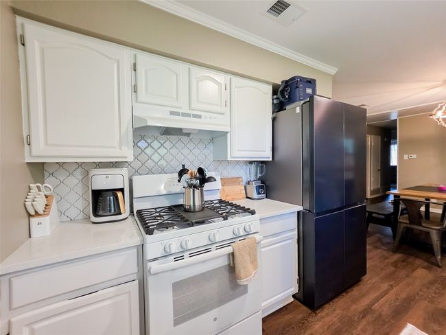 Kitchen featuring white gas range oven, under cabinet range hood, freestanding refrigerator, crown molding, and decorative backsplash | Image 24