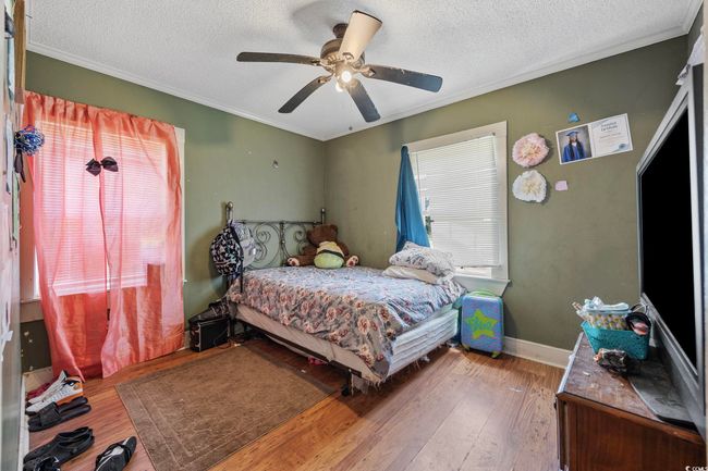 Bedroom featuring a textured ceiling, ornamental molding, wood finished floors, and a ceiling fan | Image 5