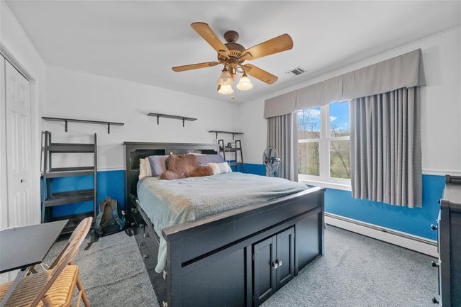Carpeted bedroom featuring baseboards, baseboard heating, a ceiling fan, and visible vents | Image 21
