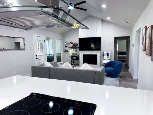 Kitchen with vaulted ceiling, ceiling fan, a large fireplace, cooktop, and wood-type flooring | Image 5