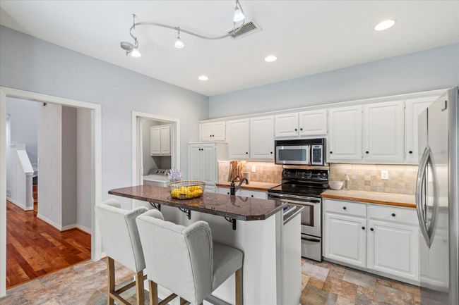 Kitchen with appliances with stainless steel finishes, a kitchen bar, backsplash, white cabinets, and light stone finish floors | Image 10