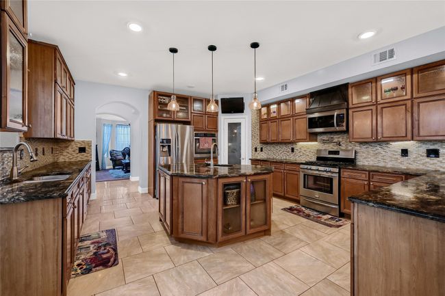 Kitchen featuring sink, backsplash, an island with sink, decorative light fixtures, and appliances with stainless steel finishes | Image 13