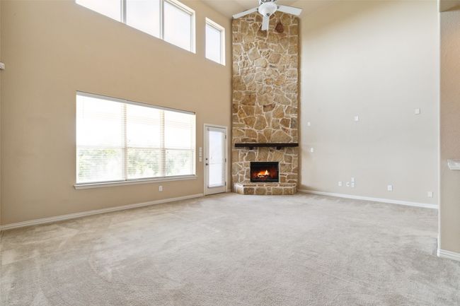 Unfurnished living room featuring a ceiling fan, carpet, a fireplace, a high ceiling, and baseboards | Image 9