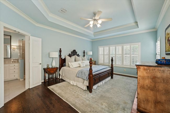 Bedroom featuring a raised ceiling, wood finished floors, crown molding, baseboards, and a ceiling fan | Image 22