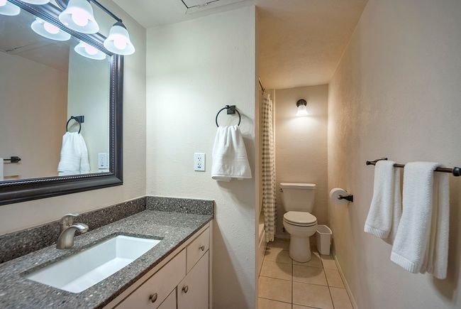 A minimalist wet room layout showcasing a vanity unit with stylish lighted mirror on the wall, towel racks, a bathtub and a toilet. | Image 17