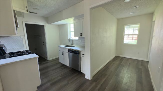 Kitchen with a textured ceiling, stainless steel dishwasher, white cabinetry, and dark wood-type flooring | Image 22