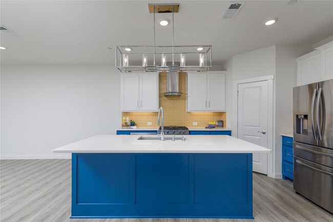 Kitchen with stainless steel fridge, wall chimney range hood, light wood finished floors, light countertops, and recessed lighting | Image 9