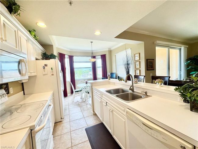 Kitchen with light countertops, white appliances, ornamental molding, a sink, and light tile patterned flooring | Image 12