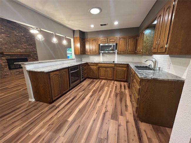 Kitchen featuring appliances with stainless steel finishes, a fireplace, light stone countertops, wood finished floors, and tasteful backsplash | Image 16