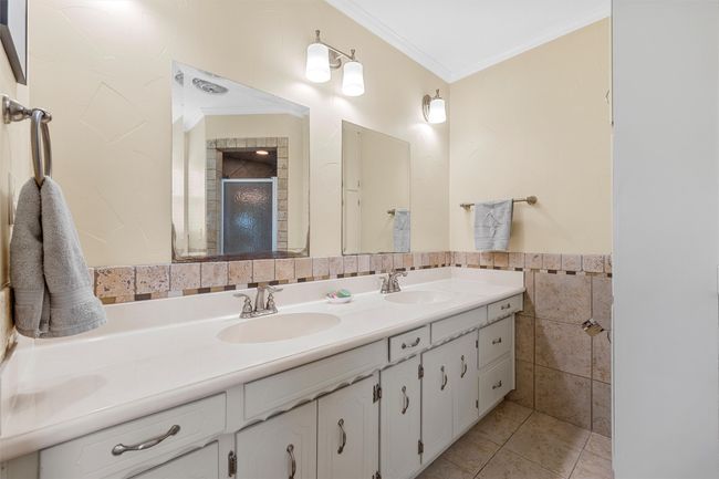 Bathroom featuring double vanity, tile walls, a stall shower, crown molding, and tile patterned floors | Image 17