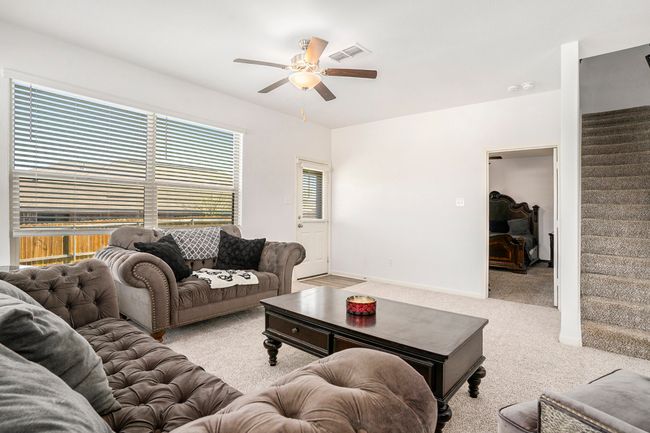 Carpeted living area featuring a ceiling fan, baseboards, and stairs. | Image 5