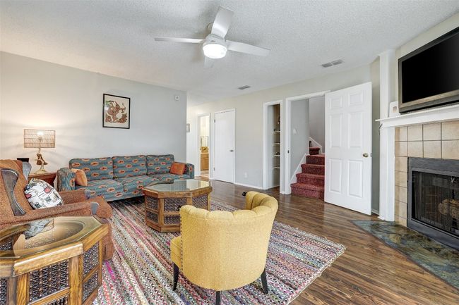 Living room with stairway, wood finished floors, a textured ceiling, a fireplace, and a ceiling fan | Image 13