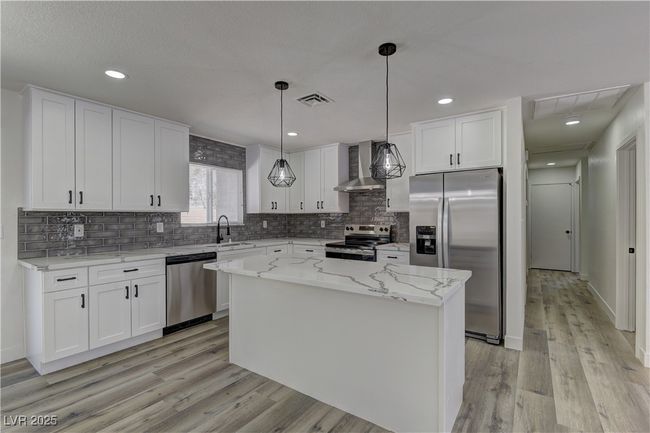 Kitchen featuring stainless steel appliances, wall chimney exhaust hood, a sink, light wood-type flooring, and white cabinetry | Image 10