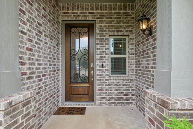 Entrance to property featuring brick columns, step up covered patio, custom door, and coach light | Image 4
