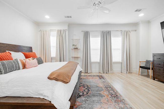 Bedroom with crown molding, cozy king bed with bedding, decorative furniture with a 75in TV, and wood finished floors | Image 17