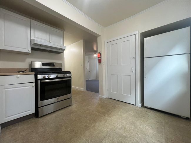Kitchen featuring stainless steel gas range, under cabinet range hood, freestanding refrigerator, ornamental molding, and white cabinetry | Image 5